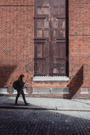 女性在黑色外套和黑色裤子走在路附近的棕色砖砌建筑