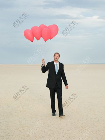 在沙漠中拿着气球奔走的商业男人图片