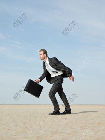 提着皮箱在沙漠中奔跑的外国商业男人图片
