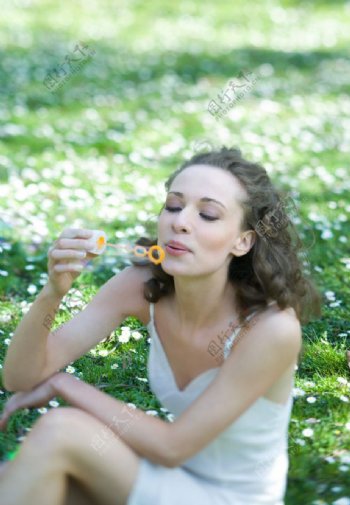 坐在绿草地上吹泡泡的快乐美女图片