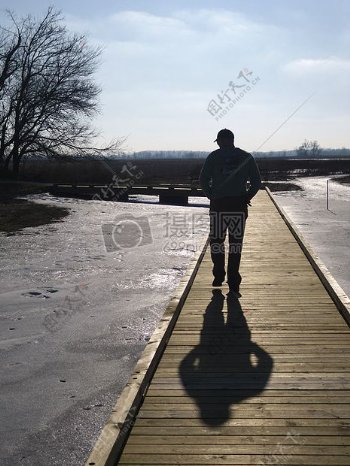 公园里阳光下独自行走在湖边的人