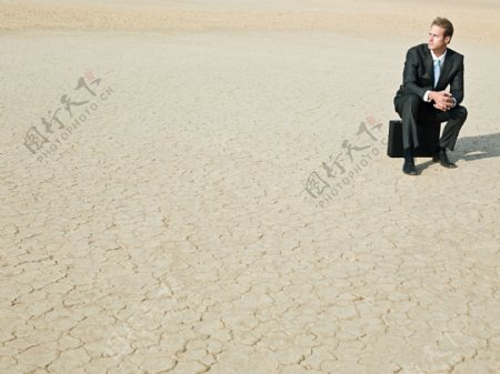 坐在裂缝土地上遥望的外国商业男人图片